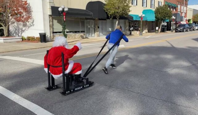 A woman pulling a sleigh where Santa Claus seats