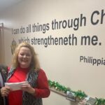 Sheriff Jody Greene presents a donation to community CPR's Christmas relief efforts. the Bible verse in question is on the wall in the background, and has been used in numerous photographs.