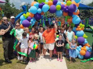 County Parks and Rec Director Julie Strickland cuts the ribbon officially opening the Trillium Play Area, with a little help from some of her closest friends.