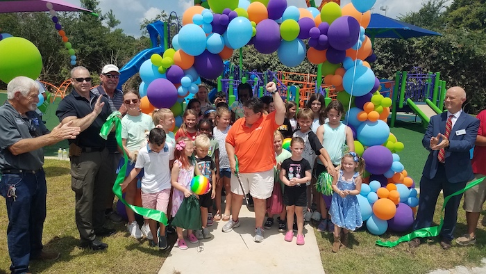 County Parks and Rec Director Julie Strickland cuts the ribbon officially opening the Trillium Play Area, with a little help from some of her closest friends.