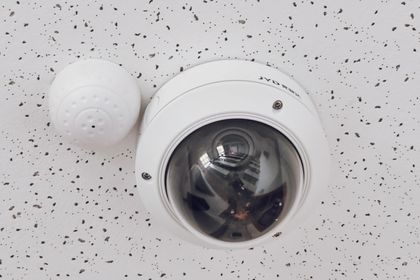 Close-up of a round dome surveillance camera installed on a speckled ceiling for security monitoring.