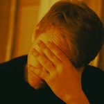 Man covering face with hand, conveying emotions in warm indoor lighting. Mental health