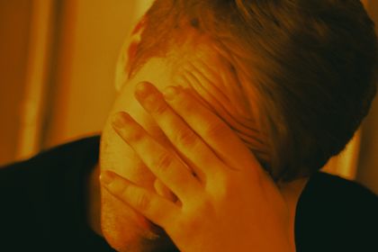 Man covering face with hand, conveying emotions in warm indoor lighting. Mental health